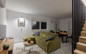 Un salon avec un canapé vert, une table à manger en bois et un escalier.