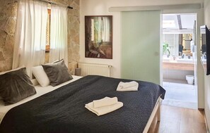 Ein Schlafzimmer mit Bett, Kissen, einem Bild, einem Heizkörper und Blick auf ein Badezimmer.