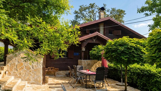 A wooden cabin with a stone wall, a dining table with chairs, and a red umbrella. - Awesome home in Slunj with sauna (Slunj)