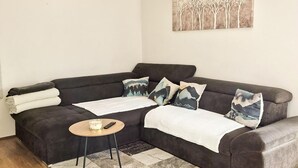 A dark-colored sofa with a white throw blanket, a small round table with a remote control, and a patterned rug. - Awesome home in Slunj with sauna (Slunj)