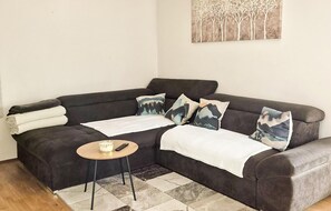 Ein dunkelgraues Sofa mit weißer Decke, ein kleiner runder Tisch mit Fernbedienung und ein gemustertes Teppich.