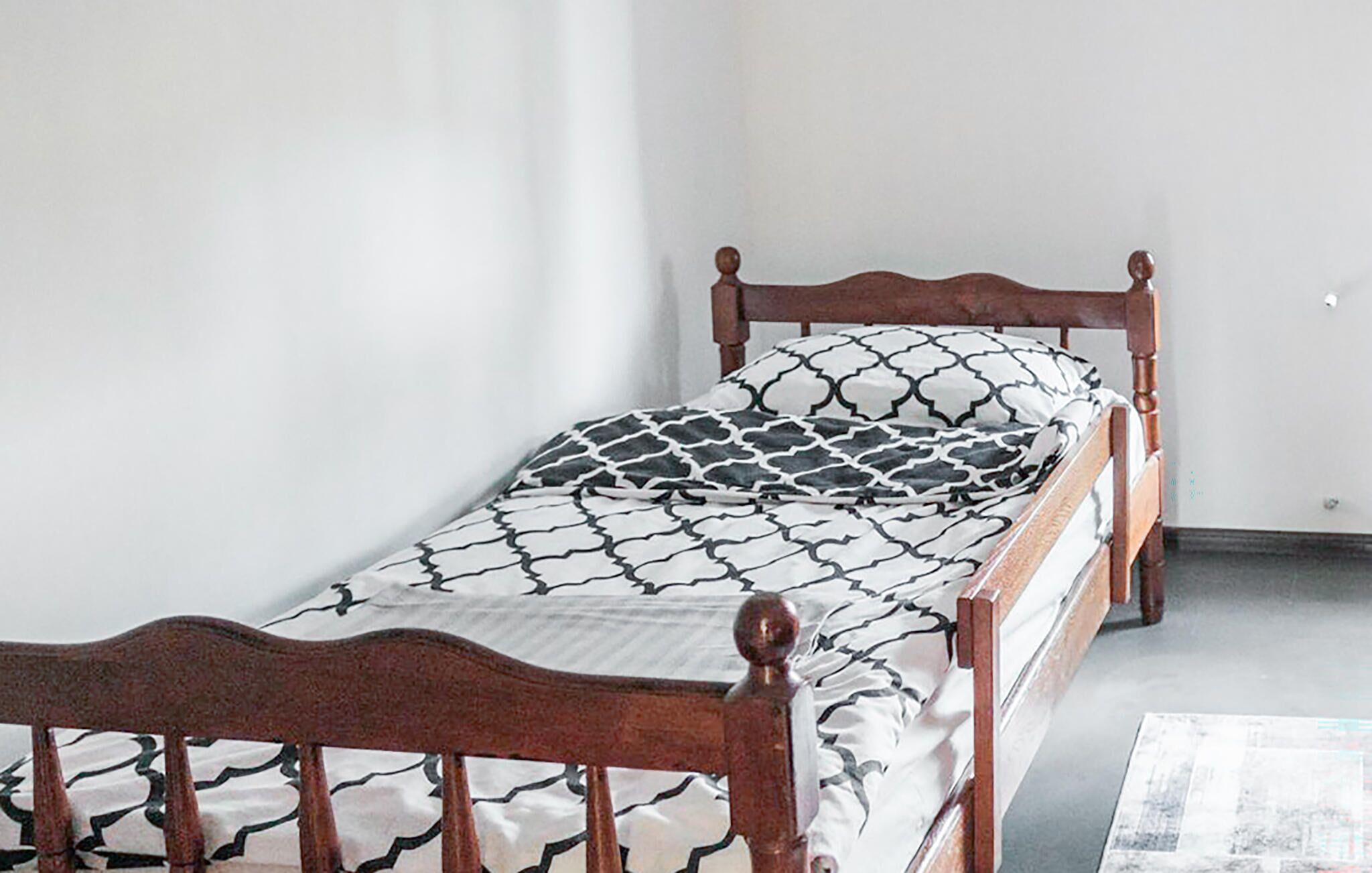 A single bed with a patterned bedspread and wooden headboard in a room with plain walls.