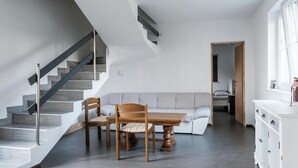Een modern interieur met een trap, een eethoek met tafel en stoelen, een bank en een kleine kitchenette.
