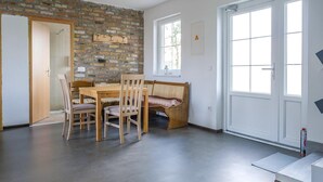 Een kamer met een bakstenen muur, een houten eettafel met stoelen, een bank, een deur en een raam.