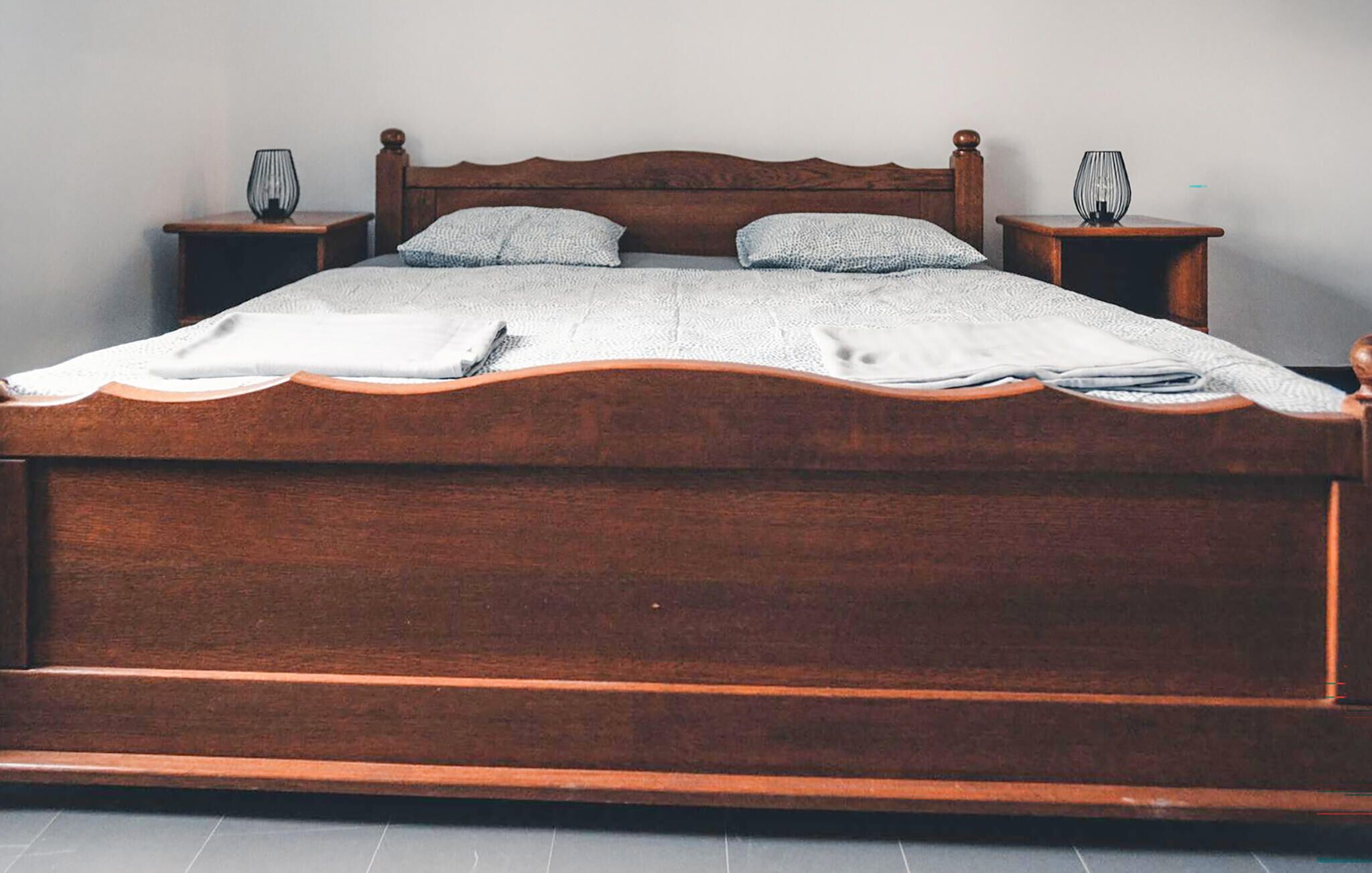 A wooden bed with a headboard, two bedside tables, and a blanket.