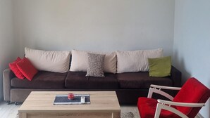 Olohuoneessa on tummanruskea sohva, puinen sohvapöytä ja punainen tuoli.