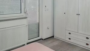 Huoneessa on sänky, patteri, vaatekaappi ja ikkuna, jossa on sälekaihtimet.
