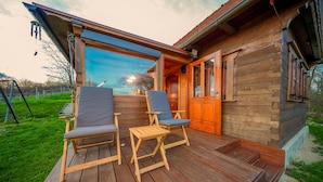 Une terrasse en bois avec deux chaises et une table, une porte en bois et une vue sur le ciel.