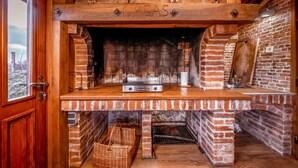 Une cheminée en briques avec un barbecue intégré, un banc en bois et un panier en osier.