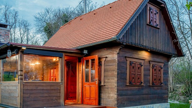 Une cabane en bois avec un toit recouvert de tuiles rouges, une porte d’entrée en verre et un petit porche.