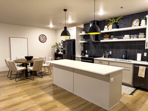 A modern kitchen with a central island, pendant lights, and a dining area with chairs.