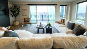 A modern living room with a sectional sofa, a small coffee table, a potted plant, and a chair. - Luxury Condo Downtown Fargo (Fargo)
