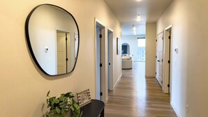 A hallway with a round mirror, a console table with a plant, and doors leading to rooms. - Luxury Condo Downtown Fargo (Fargo)