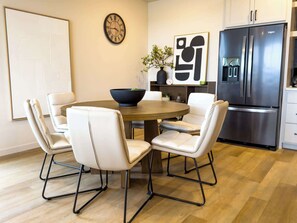 A modern kitchen with a dining table, chairs, a clock, a refrigerator, and abstract art on the wall.