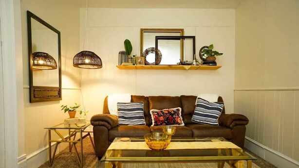 Ein Wohnzimmer mit einem braunen Sofa, einem Glastisch, einem kleinen Beistelltisch und einem Spiegel an der Wand.