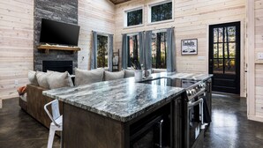 A modern kitchen with a large island, built-in oven, and a flat-screen TV. - Timbuktu with You: Hot Tub, Foosball, WiFi, Pet Friendly (Broken Bow)