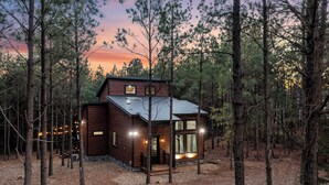 A two-story cabin with a metal roof, surrounded by tall pine trees. - Timbuktu with You: Hot Tub, Foosball, WiFi, Pet Friendly (Broken Bow)