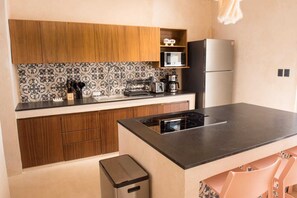 Eine kleine Küche mit Holzausstattung, einer schwarzen Arbeitsplatte, einer eingebauten Mikrowelle, einer Kaffeemaschine und einem Edelstahlkühlschrank.