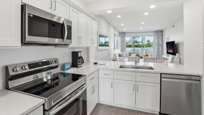 A modern kitchen with stainless steel appliances, white cabinetry, and a large window offering a view of the outdoors. - #1516 - Amazing Golf and Lake View in Luxury Villa (Naples)