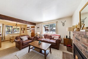 A living room with leather sofas, a wooden coffee table, a fireplace, and a large window. - Tahoe Cabin Near Slopes & Lake 3BR 2BA (South Lake Tahoe)