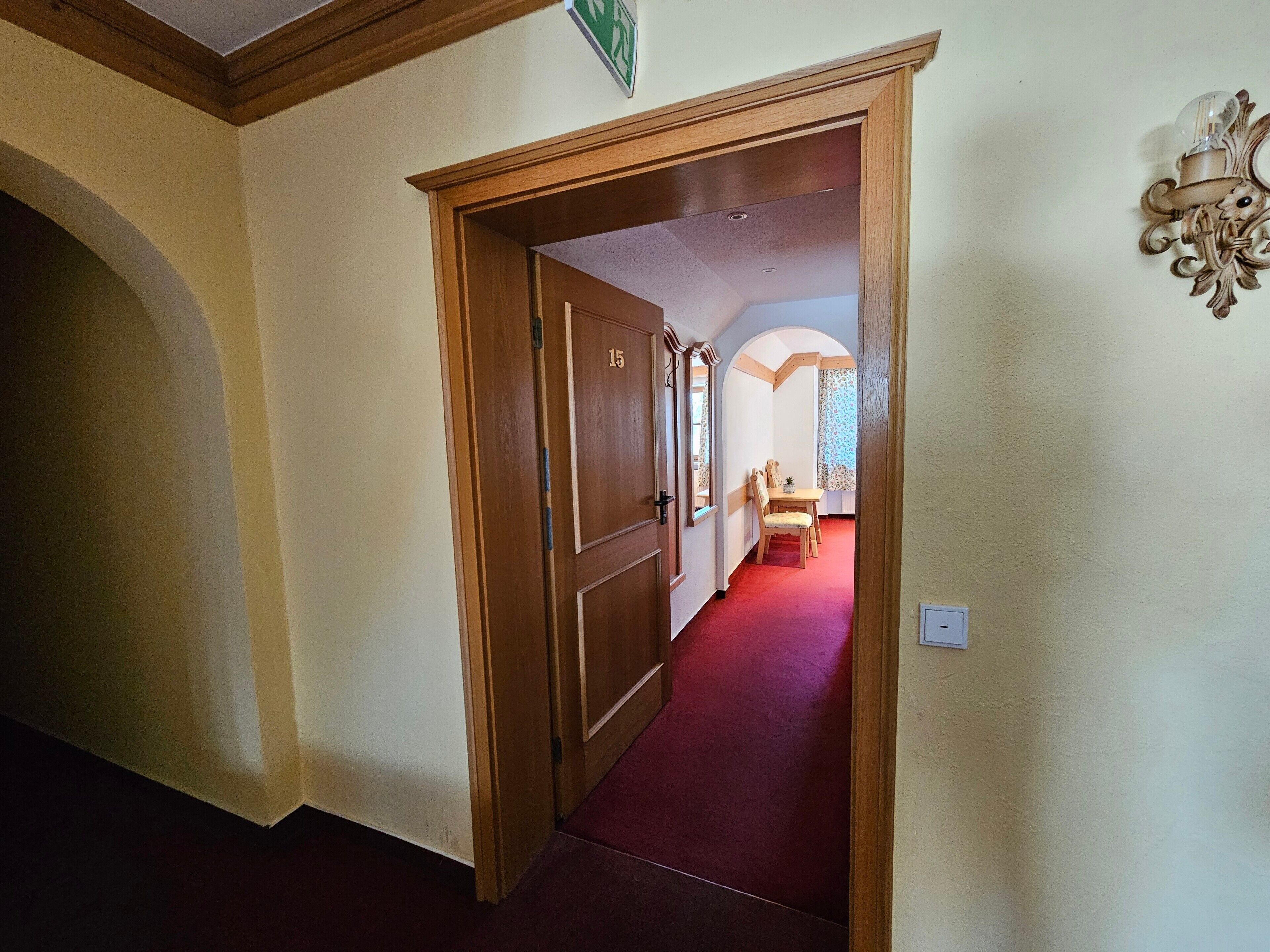 A hallway with a wooden door, a red carpet, and a dining area with a table and chairs.