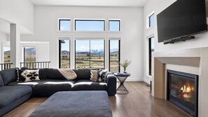 En moderne stue med en modulsofa, en pejs og store vinduer med udsigt til et bjerglandskab.