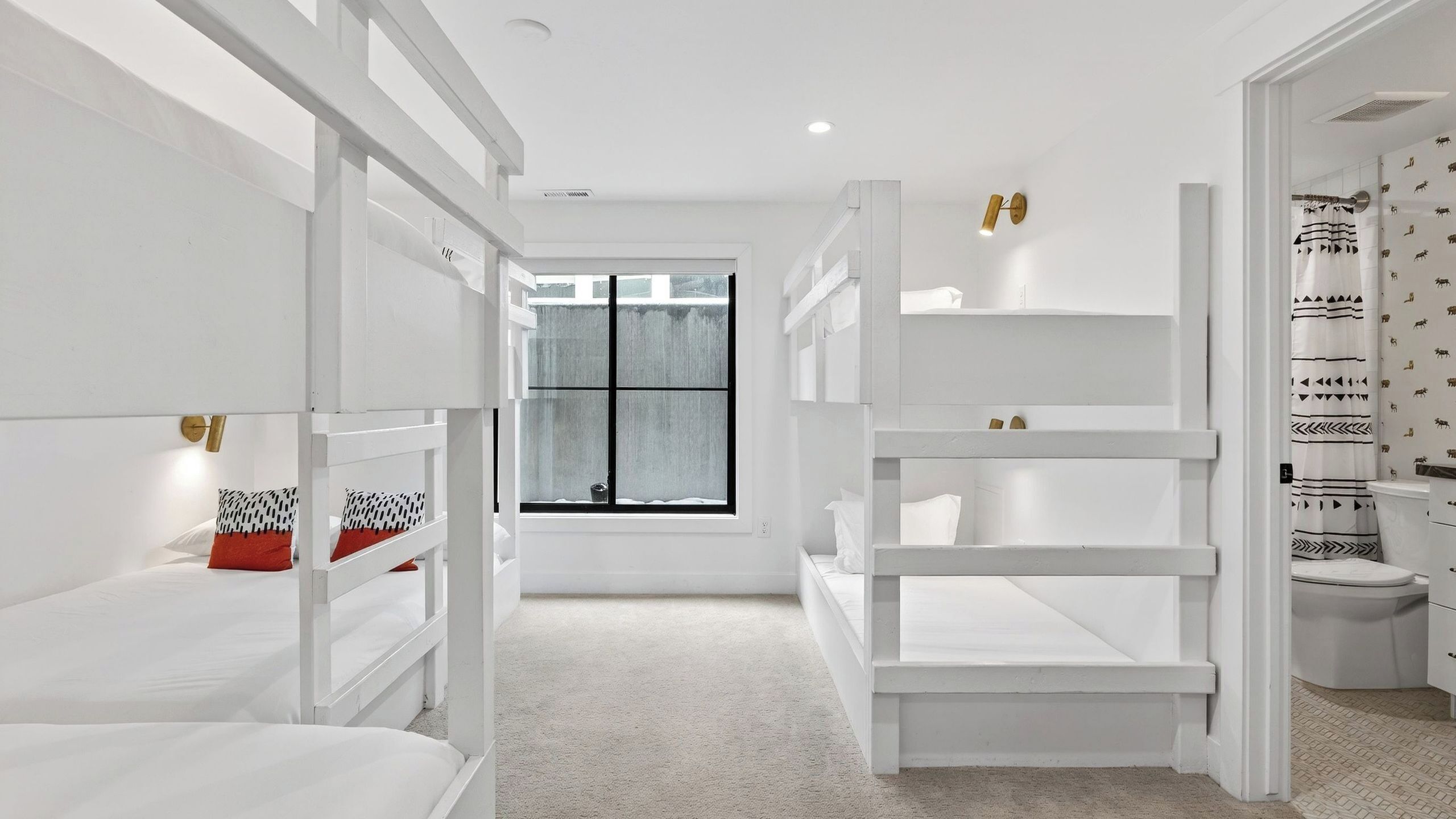 Un dormitorio moderno con una decoración en tonos blancos, camas literas, un ventanal grande y un baño con papel tapiz estampado.