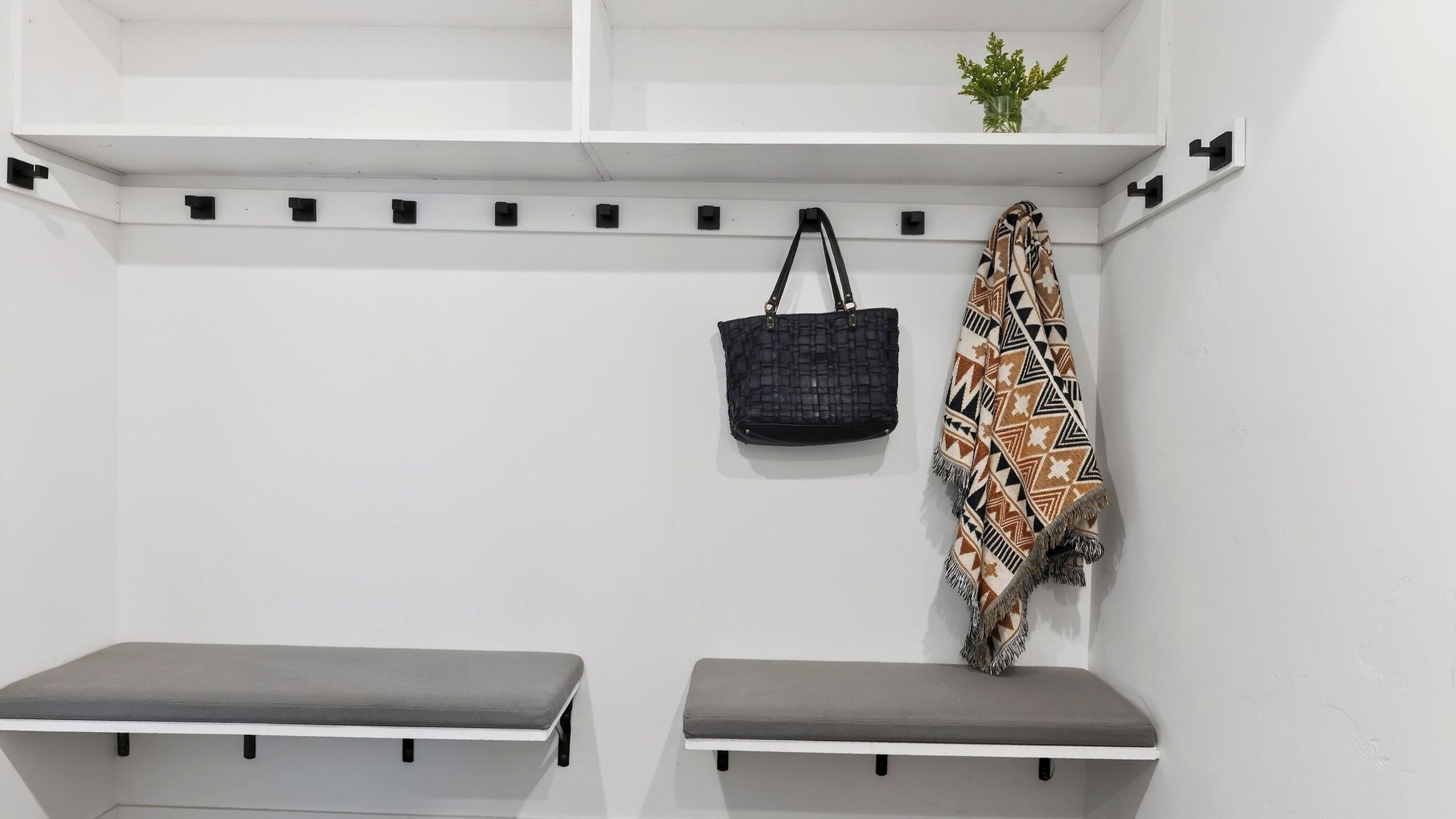 A white locker room with two grey benches, a black woven bag, and a patterned scarf hanging on the wall.