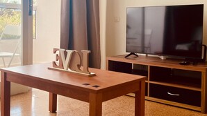 Ein Wohnzimmer mit Holztisch, Flachbildfernseher und einer Schiebetür zu einem Außenbereich.