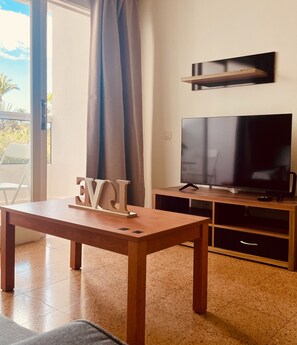 A living room with a wooden table, a flat-screen TV, and a sliding glass door leading to an outdoor area. - Golden Stay in Maspalomas (San Bartolomé de Tirajana)
