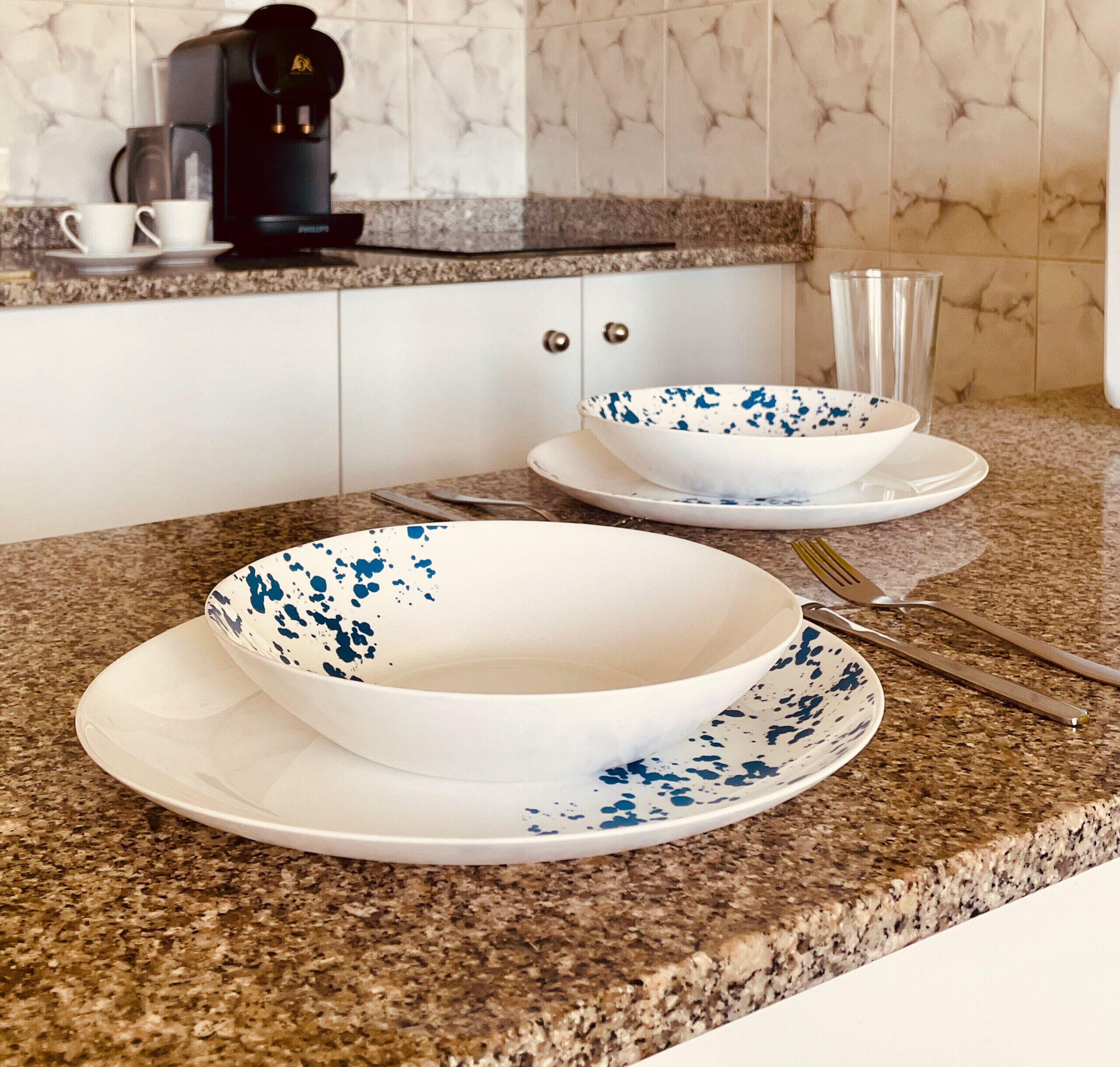 A kitchen with granite countertops, white cabinets, a coffee maker, and two bowls with blue speckles on white plates.