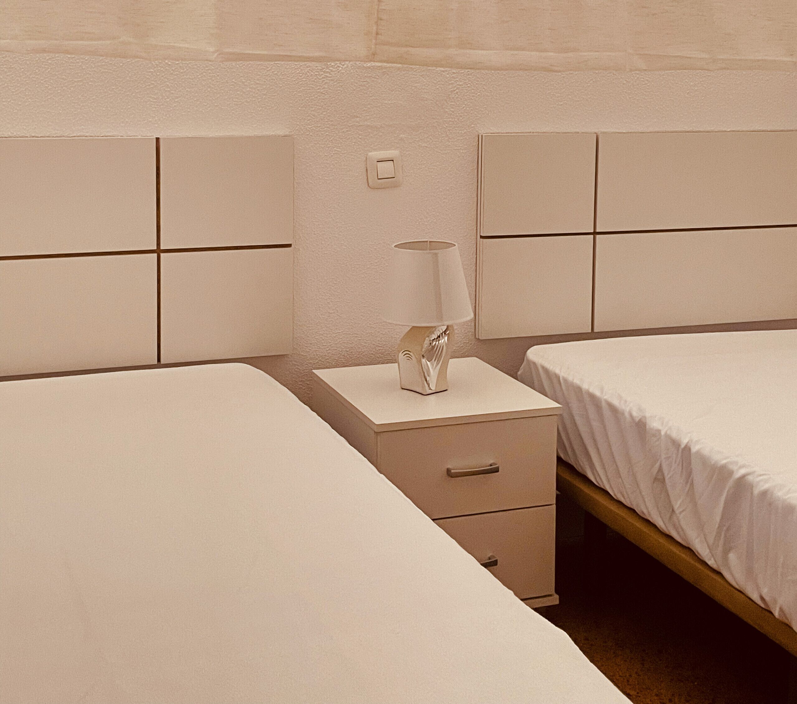 Une chambre d’hôtel avec deux lits, une table de chevet avec une lampe et un interrupteur fixé au mur.