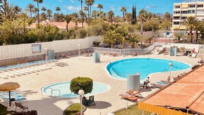 Ein Resort mit großem Pool, Liegestühlen, Palmen und blauem Himmel.