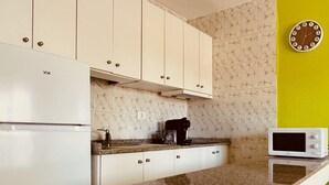Eine Küche mit weißen Schränken, einer Granit Arbeitsplatte, einer Kaffeemaschine, einer Mikrowelle und einer Wanduhr.