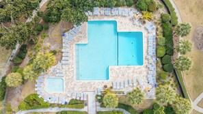 Vue aérienne d’un complexe hôtelier doté d’une piscine centrale, entourée d’espaces de détente et de jardins aménagés.