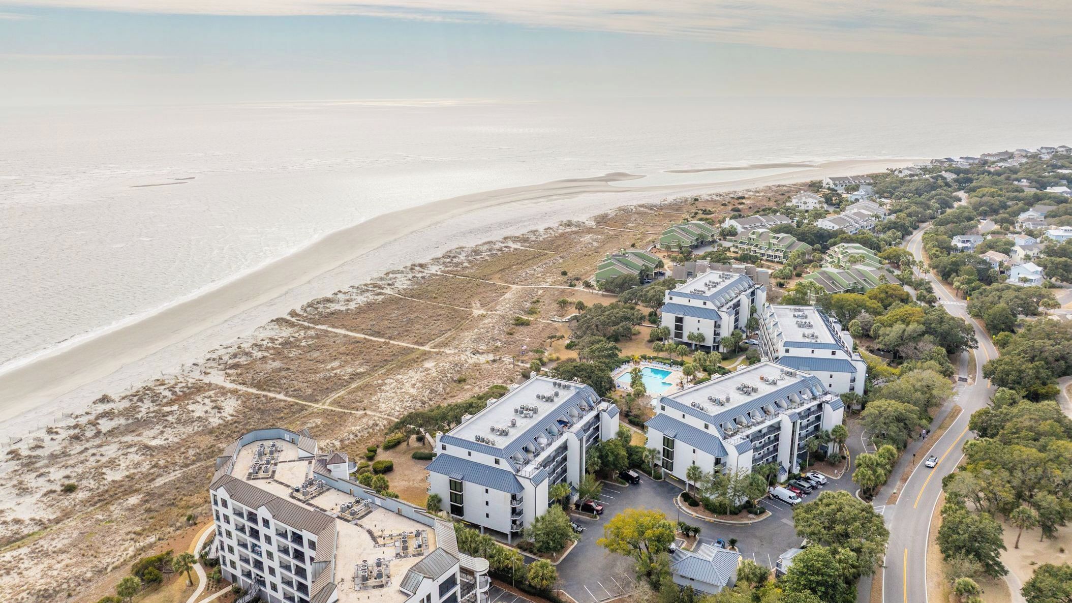 Ein Küstenhotel mit mehreren Gebäuden, einem Strand und einem Parkplatz.