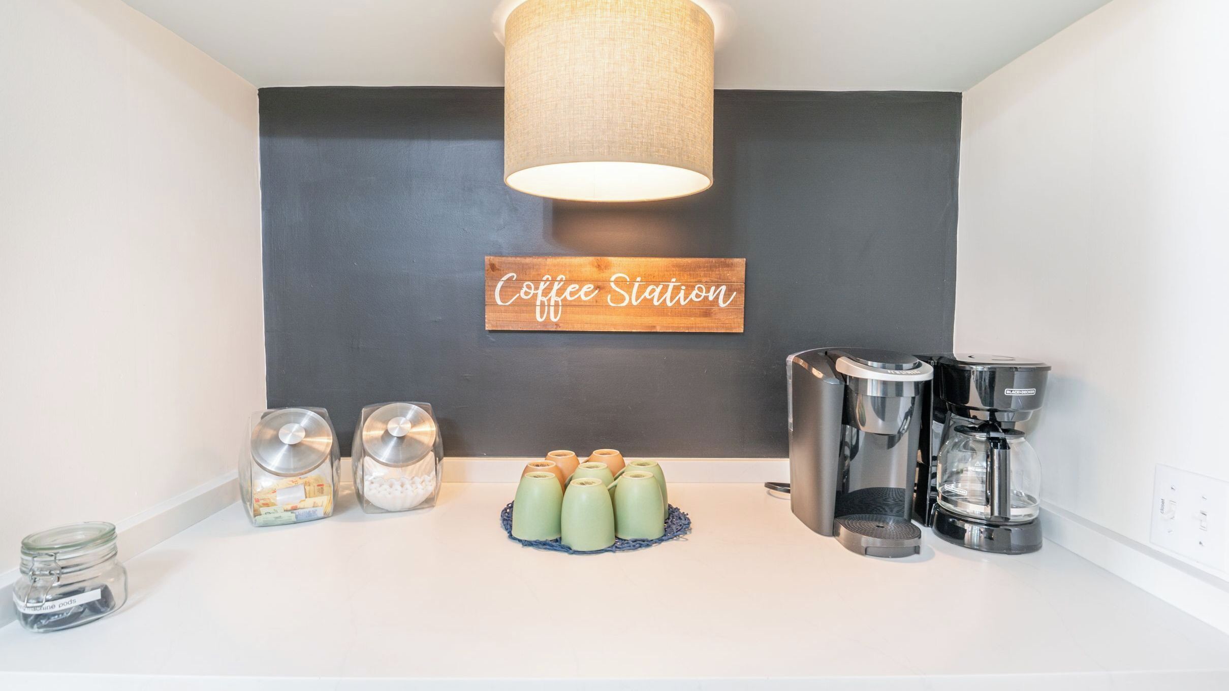 Een koffiehoek met een bordje, koffiezetapparaten en theepotten.
