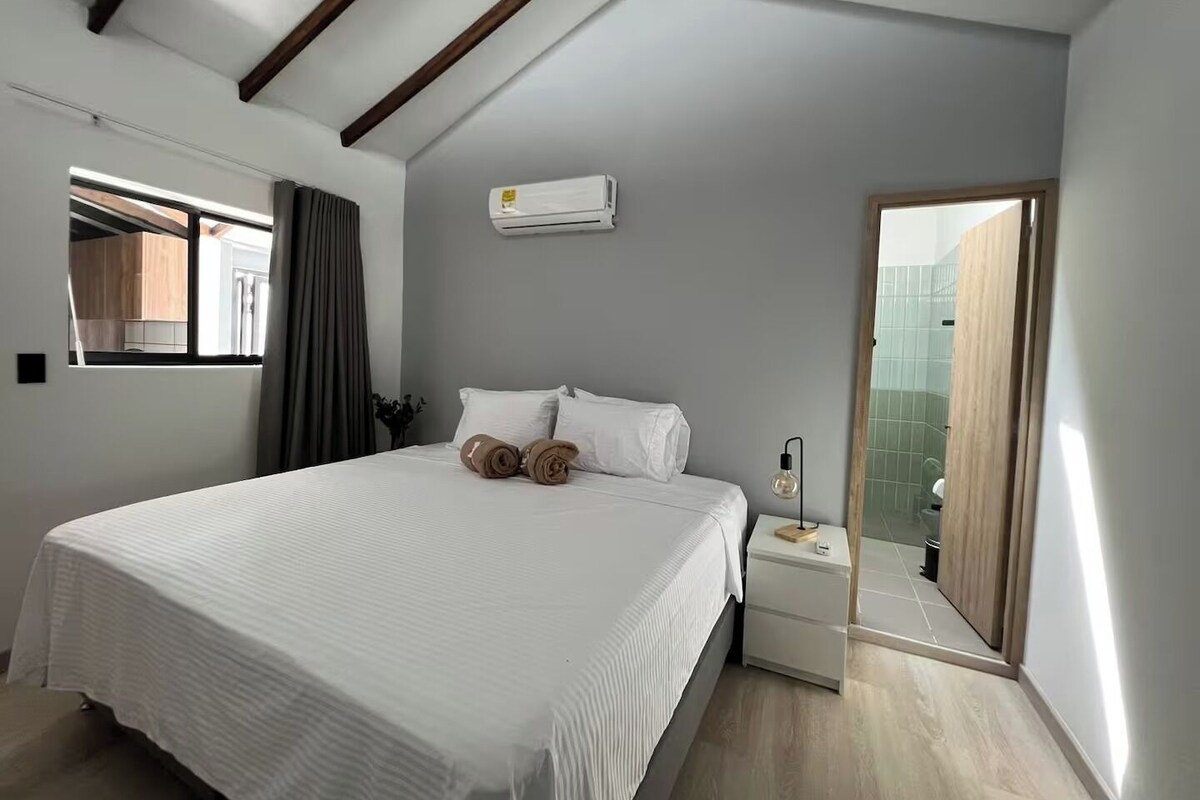 A bedroom with a bed, a nightstand, a window, and an air conditioning unit.