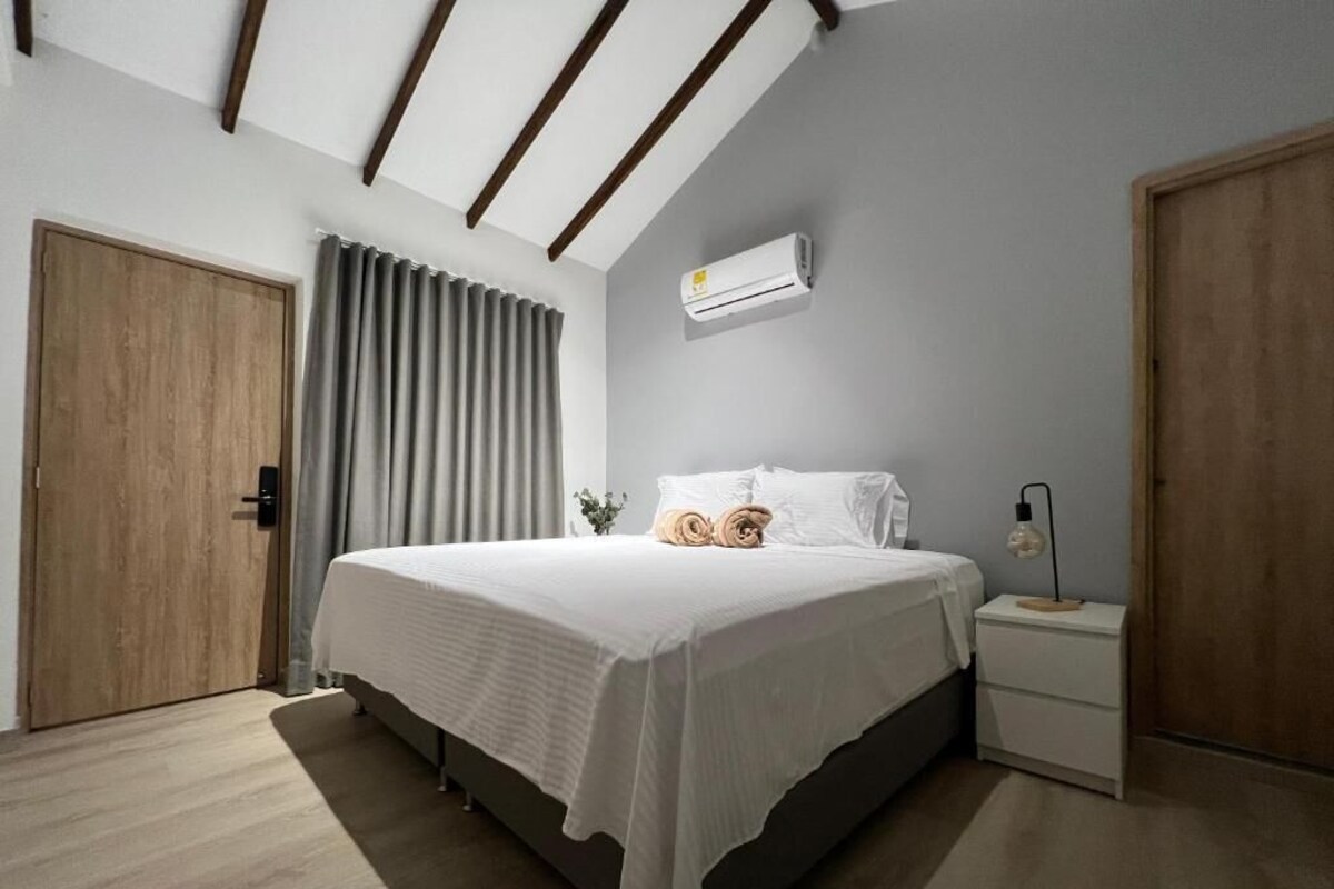 A bedroom with a bed, bedside table, nightstand, and an air conditioning unit.