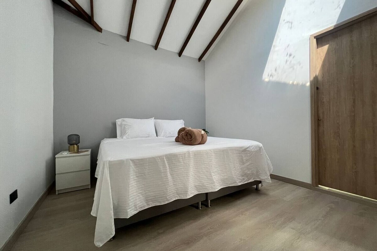 A bedroom with a bed, a nightstand, a wooden wardrobe, and a skylight.