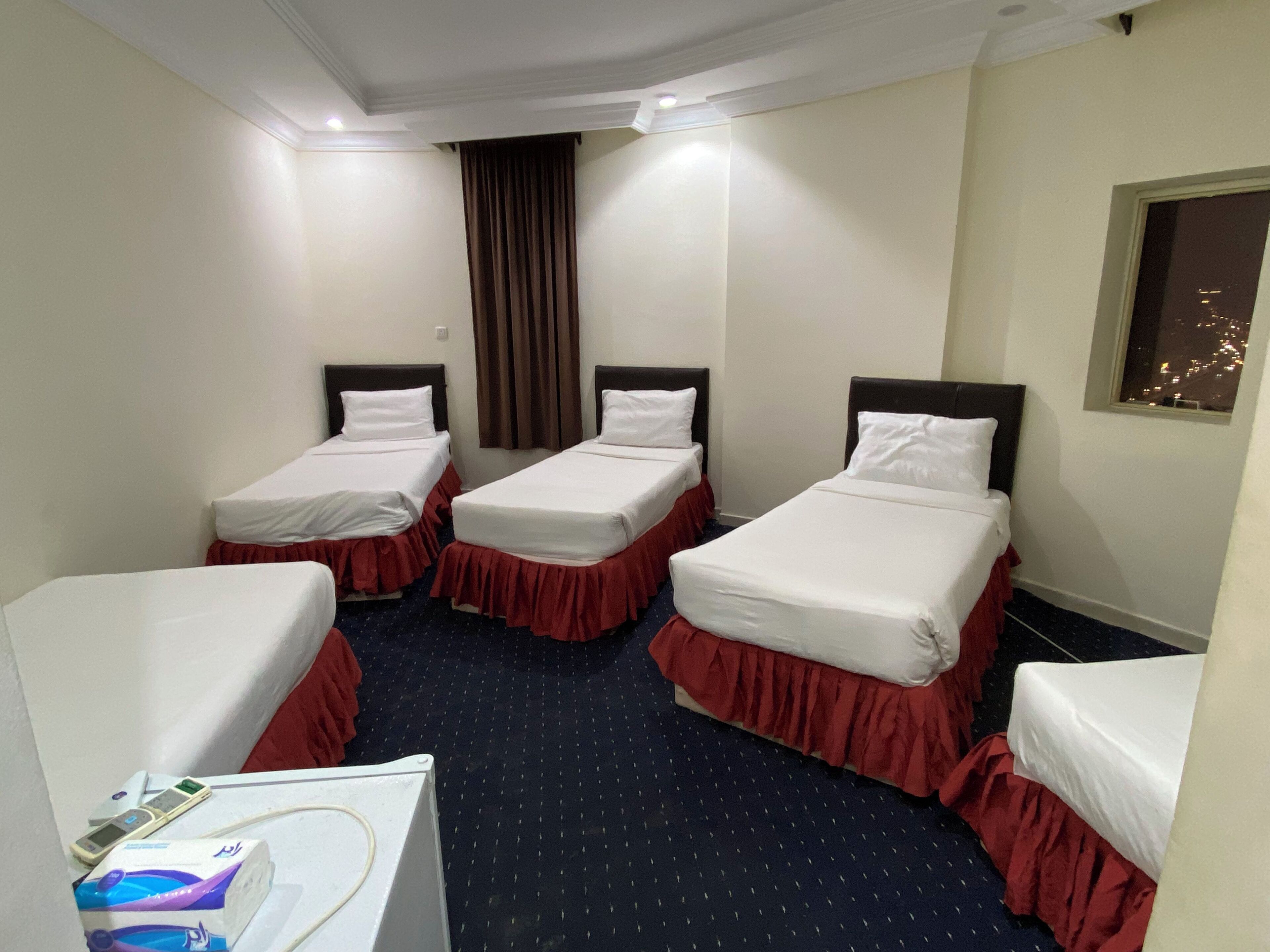 A hotel room with three single beds, a small desk, and a window with a city view.