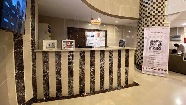 A hotel reception desk with a check-in counter, a digital screen, and a QR code sign. - nazal alroh alhora -Hajj Street (Makkah)