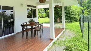 An outdoor patio with a wooden table and chairs, a hanging basket, and a view of a green garden. - Bungalow Hoarai Uturoa (Uturoa)