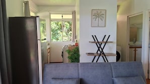 A living room with a grey sofa, a black refrigerator, and a kitchen area visible through an open door. - Bungalow Hoarai Uturoa (Uturoa)