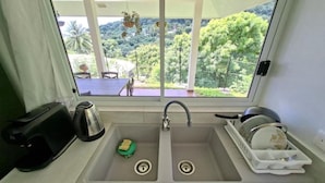 A kitchen with a double sink, a coffee maker, a dish rack, and a view of greenery outside. - Bungalow Hoarai Uturoa (Uturoa)