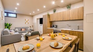 A modern kitchen with wooden cabinets, a dining table set with plates, glasses of orange juice, and a croissant. - Spacious Apartment - 2br/10p - Place D'italie (Paris)