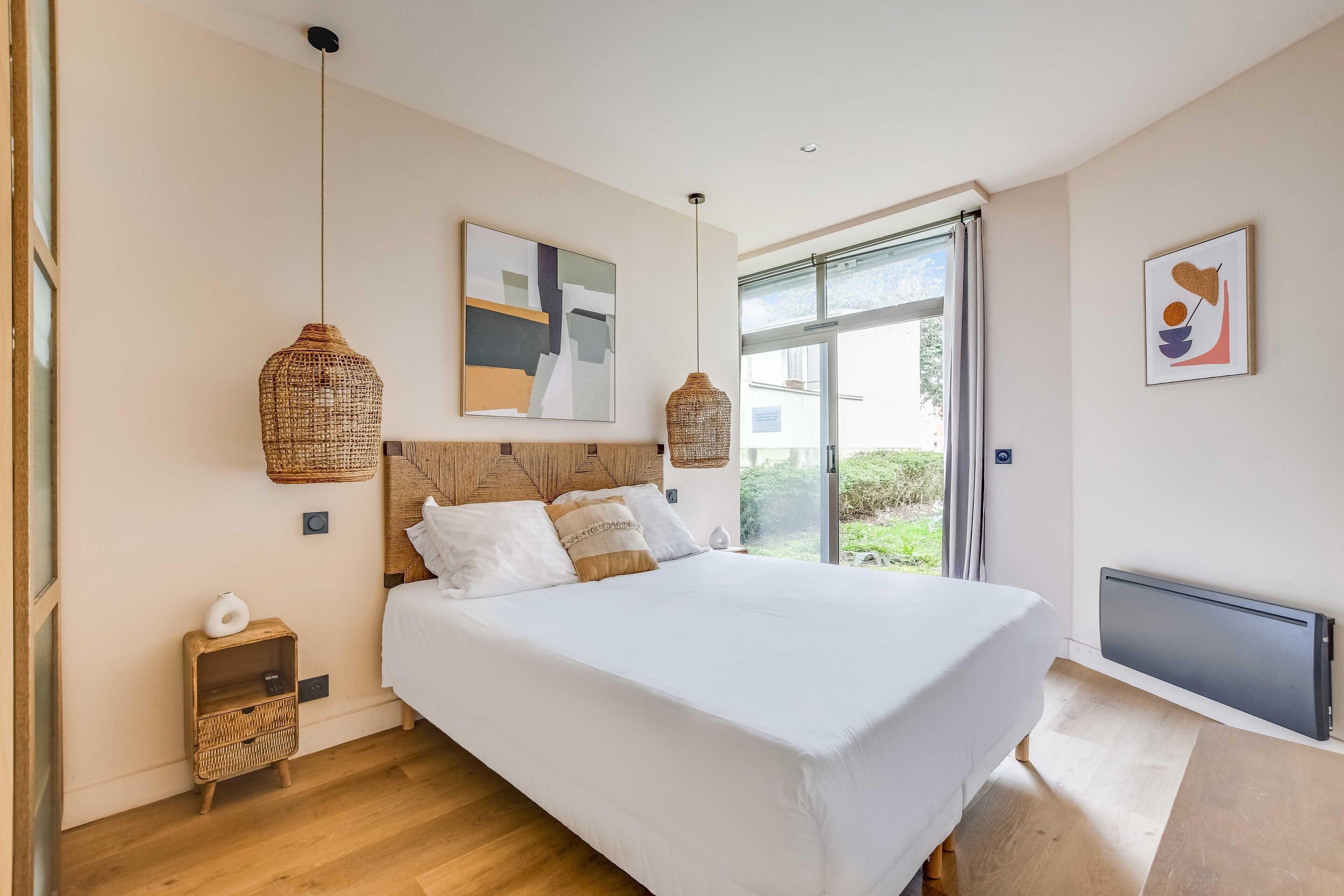 Ein modernes Schlafzimmer mit einem großen Bett, Blick auf Grünflächen und einer Deckenleuchte.