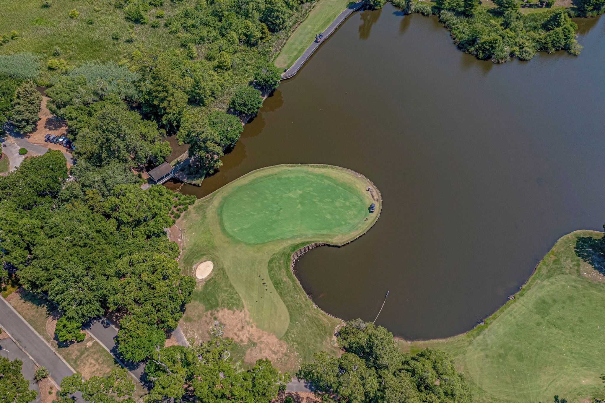 An aerial view of a golf course with a pond, surrounded by dense trees and a road.