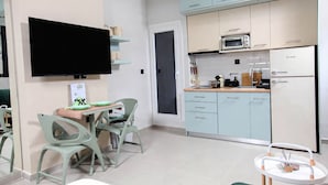 Cocina moderna con armarios azul claro, un microondas y un refrigerador. Hay un comedor con mesa y sillas, y un televisor de pantalla plana montado en la pared.