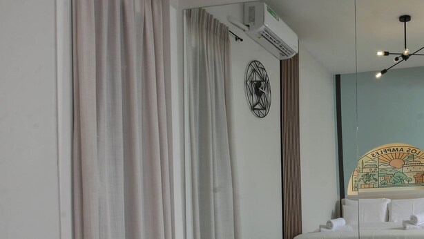 Habitación de hotel con cama, espejo, ventana con cortinas, equipo de aire acondicionado e iluminación en el techo.